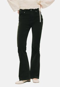 Jeans neri svasati in un materiale morbido, con vita aderente, design a cinque tasche e dettagli di cucitura discreti, abbinati a scarpe chiare.