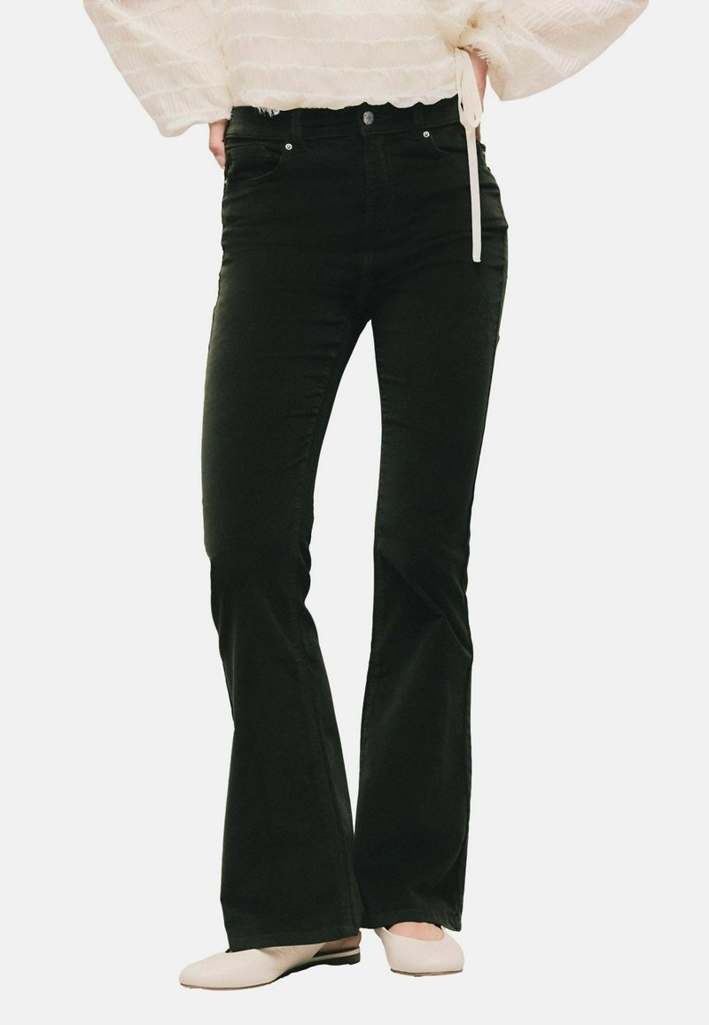 Jeans neri svasati in un materiale morbido, con vita aderente, design a cinque tasche e dettagli di cucitura discreti, abbinati a scarpe chiare.