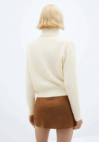 Maglione a collo alto a coste color crema con vestibilità cropped, abbinato a una mini gonna in suede marrone, visto di spalle.