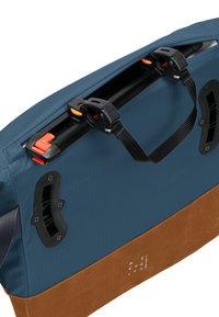 Borsa di tessuto blu con base marrone, dotata di hardware nero, spallacci regolabili e dettagli arancioni per la chiusura. La scritta recita 'RICICLATO.'