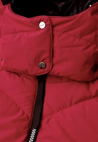 Chaqueta acolchada roja con cuello alto, que cuenta con botones de presión y un cierre frontal. La tela es suave con una textura acolchada.