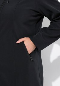 Czarna kurtka o gładkiej fakturze, z kieszenią na zamek z boku. Projekt obejmuje wysoki kołnierz i długie rękawy.