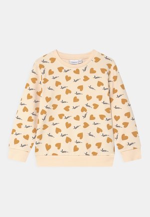Sweat-shirt pour enfants à manches longues de couleur crème, orné de cœurs marron et du mot "love" écrit en écriture cursive noire sur tout le tissu.