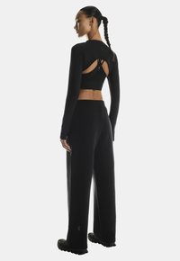 Black long-sleeve top with cut-out back paired with matching black high-waisted pants. Material appears smooth with a fitted design.