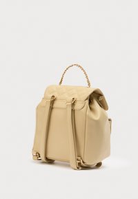 Μπεζ σακίδιο πλάτης από δερματίνη με καπιτονέ επάνω μέρος, χειρολαβή με αλυσίδα και διπλούς ιμάντες ώμου. Μαλακή υφή και μινιμαλιστικός σχεδιασμός. Διακοσμητικά στοιχεία σε χρυσό τόνο.
