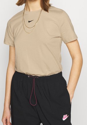 Osoba nosząca beżowy T-shirt Nike i czarne spodnie Nike ze różowym sznurkiem, ozdobiona dwoma złotymi łańcuszkami.