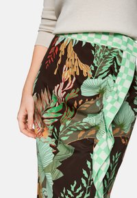 Blumenmusterrock mit dunklem Hintergrund, der lebendige grüne und rote Blätter zeigt, und einem mintgrünen karierten Stoffakzent an der Taille.