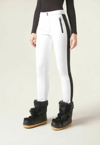 Vita slim fit-byxor med svarta sidosträck och dragkedjefickor, matchade med svarta pälsbeklädda platåskor. Slät tyg med en elegant finish.