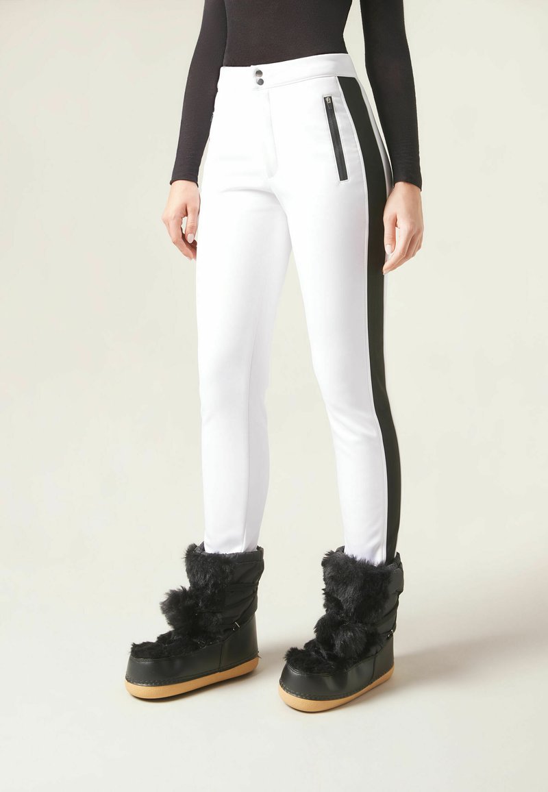 Vita slim fit-byxor med svarta sidosträck och dragkedjefickor, matchade med svarta pälsbeklädda platåskor. Slät tyg med en elegant finish.