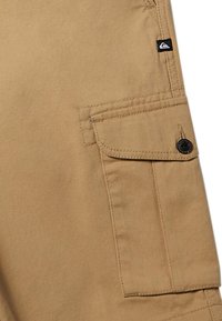 Shorts cargo beiges en coton avec une poche avant à bouton, des poches latérales et une petite étiquette noire sur la ceinture.
