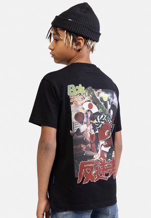 Jongen draagt een zwarte muts en een t-shirt met een kleurrijke Japanse afbeelding waarop gebouwen, Godzilla en personages die een Japanse vlag vasthouden te zien zijn.