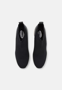 Scarpe slip-on nere con tomaia in maglia testurizzata, con un colletto a forma di V e una suola in gomma di colore chiaro. Decorate con un tallone grigio.