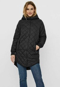 Giacca lunga nera trapuntata con cappuccio, caratterizzata da motivi a diamante, chiusura frontale con bottoni automatici e tasche laterali con zip. Materiale morbido e leggero.