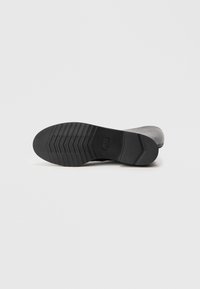Suela de zapato negra hecha de goma, con un patrón de relieve texturizado que presenta surcos horizontales y diagonales para mejorar la tracción.