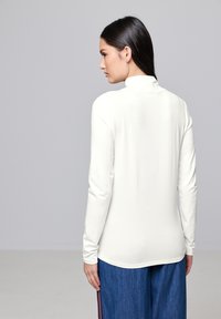 Witte langemouwen top met een hoge kraag, strakke pasvorm en gladde textuur. Gecombineerd met losse denim broeken met zijstrepen.