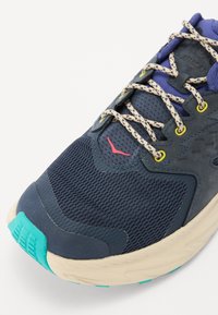 Scarpa da corsa navy con tomaia in rete e accenti in gomma. Presenta una suola beige, un tallone azzurro chiaro e lacci a contrasto beige e navy.