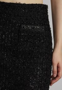 Falda negra texturizada de tweed con un patrón tejido, que presenta un pequeño bolsillo adornado con cuentas negras y un ribete negro suave.