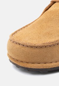 Καφέ παπούτσι από σουέτ σε ανοιχτή απόχρωση, με στρογγυλεμένη μύτη, ορατές ραφές κατά μήκος της άκρης και υφασμένο καουτσούκ σόλα.