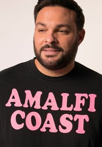 Camiseta negra con un gran texto rosa que dice "COSTA DE AMALFI". Cuello clásico de estilo crew, mangas cortas, textura de tela suave.