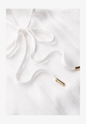 Tissu texturé blanc avec un cordon de serrage noué et des accents métalliques dorés. Le tissu présente un motif subtil, ajoutant de la dimension au design.