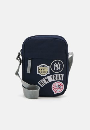 Sac de bandoulière en tissu marine avec une sangle grise, mettant en avant quatre écussons brodés, dont "New York" et des designs sur le thème de New York.