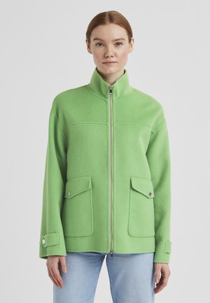 Grüne Fleecejacke mit hohem Kragen, Frontreißverschluss und zwei geknöpften Taschen. Hat eine dicke Textur und eine lockere Passform.