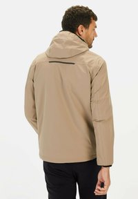 Lichtbeige jas met capuchon, voorzien van een ritssluiting aan de voorkant, elastische manchetten en een zwart accentstreep op de achterkant. Gladde textuur, ontwerp voor buiten.