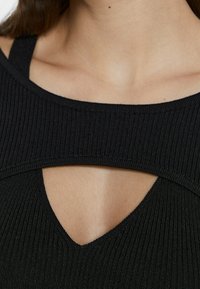 Haut noir côtelé avec larges bretelles et une découpe en forme de V au niveau de l'encolure, présentant un tissu texturé avec une coupe ajustée.