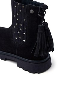 Botín negro de ante hasta el tobillo con un diseño texturizado, que presenta acentos de estrellas plateadas, un detalle de borlas y una suela de goma gruesa.