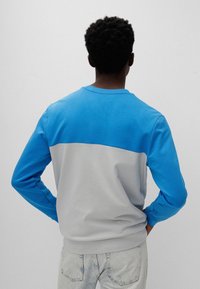 Sweatshirt mit Rundhalsausschnitt in Blau und Grau, mit langen Ärmeln und einem Farbblockdesign. Hergestellt aus weichem Stoff mit glatter Textur.