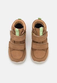 Chaussures en cuir marron pour tout-petits avec deux brides Velcro et accents verts. Bout arrondi, surface texturée et semelles en caoutchouc blanc.