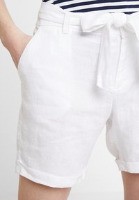 Pantaloni corti bianchi in lino con vita regolabile, dotati di tasche laterali e orli arrotolati, realizzati in un tessuto leggero e testurizzato.