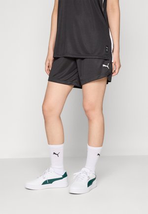 Sorte atletiske shorts og ermeløs top med hvide detaljer, parret med hvide sneakers med grønne elementer og sokker i crew-længde.