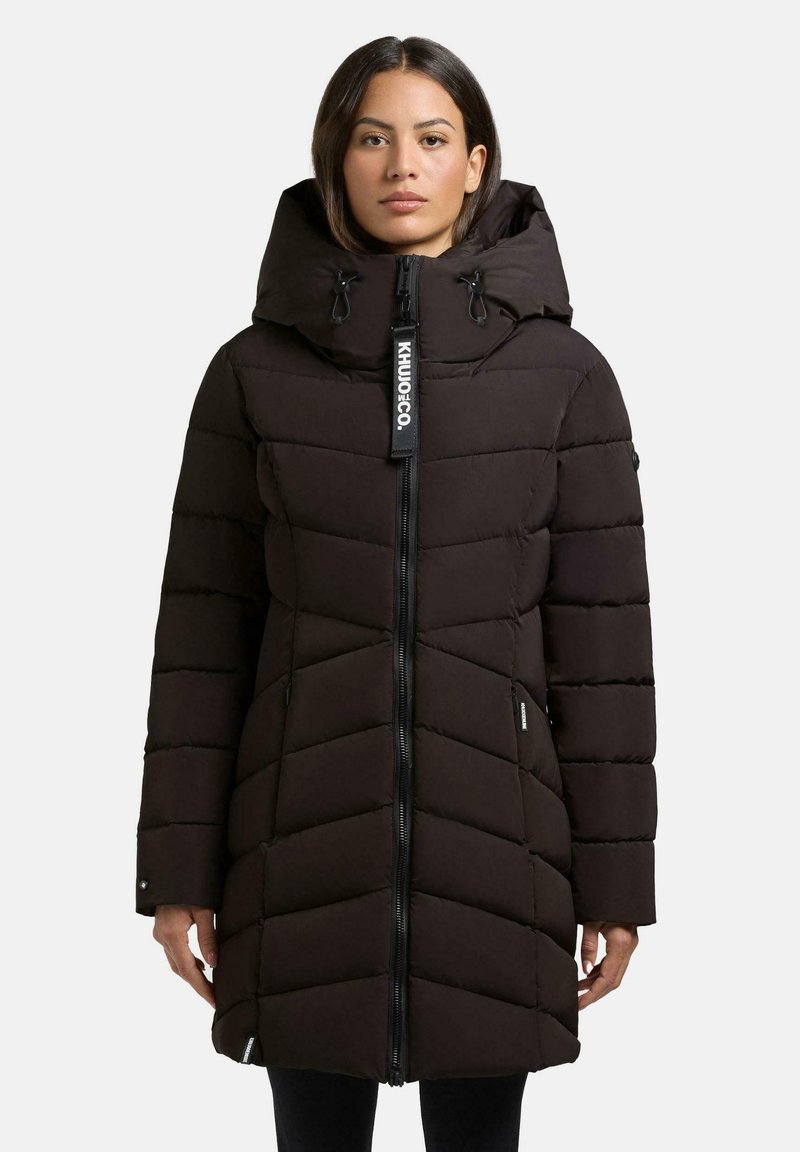 Cappotto invernale imbottito nero con colletto alto, zip frontale e tasche laterali. Presenta cuciture diagonali e un'etichetta con logo sulla zip.