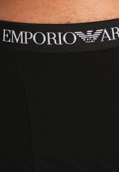 Črne spodnjice z širokim elastikastim pasom z logotipom "EMPORIO ARMANI" v beli barvi, gladka tekstura in tesno prileganje.