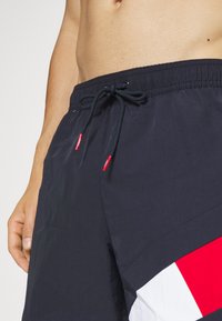Marine svømmeshorts med elastisk liv og snøring. Har et stort geometrisk preg i rødt og hvitt. Lett, glatt materiale.