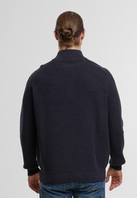 Ciemnogranatowy sweter z dzianiny o ribbowanej fakturze, z wysokim kołnierzem i luźnym krojem. Cechuje się jednolitym kolorem, bez widocznych wzorów czy akcentów.