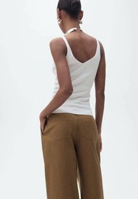 Top imbottito bianco a coste con scollo a V sul retro, abbinato a pantaloni marroni a vita alta e gamba larga con due tasche posteriori. Tessuto complessivamente liscio.