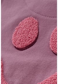 Close-up van roze getextureerde ovale vlekken genaaid op een zachte paarse stof, die de textieldetails en de stiksels benadrukt.