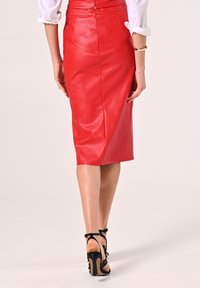 Roter Lederbleistiftrock mit glatter Textur, knielang, mit einem verdeckten Reißverschluss auf der Rückseite. Schwarze Riemchenabsätze ergänzen den Look.