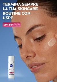 Nivea Cellular Expert Filler, flacone di plastica bianca con erogatore, con SPF 50, posizionato su uno sfondo blu vicino al viso di una donna con la pelle trattata con prodotti per la cura della pelle.