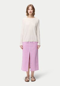 Ljusbeige långärmad topp med struktur, kombinerad med en midjelång kjol i rosa och vitt randigt mönster med en slits framtill, kompletterad med bruna sandaler.