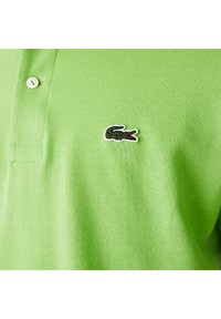 Grön polo skjorta i strukturerad tyg, med krage som kan knäppas och en broderad svart krokodil-logotyp med röd accent.