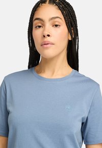 Blå bomulds T-shirt med rund halsudskæring, korte ærmer og et lille broderet logo på brystet. Glat tekstur og afslappet pasform.