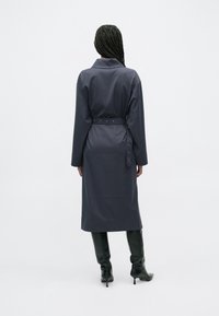 Dlhý tmavosivý kabát s opaskom v páse, s golierom a dlhými rukávmi. Hladká látka a dizajn do kolien s minimalistickým štýlom.