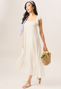 White midi dress with ruffled sleeves, square neckline, and tiered hem. Paired with a beige woven bag with yellow handles and flat sandals.