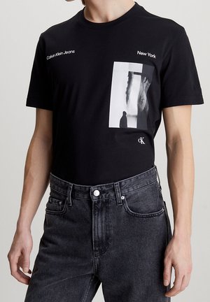 T-shirt en coton noir avec un imprimé graphique d'une image monochrome et le texte "Calvin Klein Jeans" et "New York" en blanc. Manches courtes.