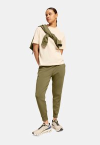 Beige bomulds T-shirt, olivengrønne joggers og cremefarvede sneakers. Sweatshirt hængende over skuldrene. Enkel, afslappet sportstøj.