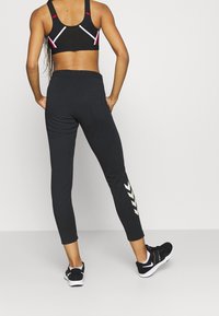 Schwarze Sportleggings mit figurbetontem Design, Knöchellänge, mit weißen Streifen entlang des Beins und kombiniert mit schwarzen Sneakern.