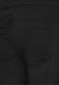 Svart tyg med en slät textur, visar en nära bild av en bakficka och sömdetaljer. Enkel design, inga synliga mönster eller detaljer.